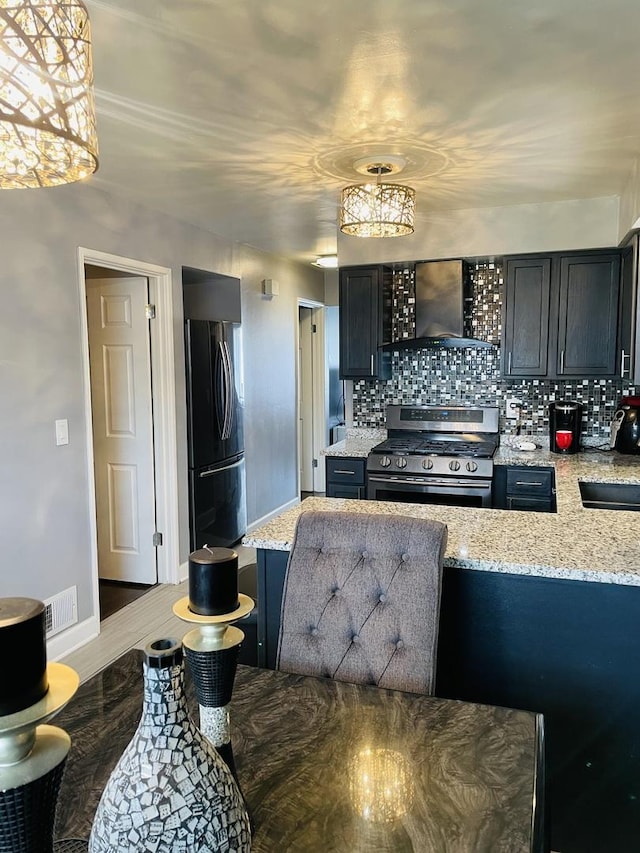 kitchen featuring tasteful backsplash, visible vents, gas range, freestanding refrigerator, and wall chimney exhaust hood
