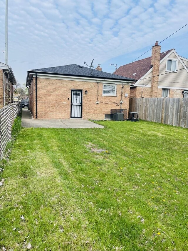 back of property with a patio area, a lawn, central AC, brick siding, and a fenced backyard