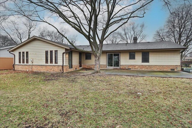 rear view of property featuring a patio, brick siding, a chimney, and a yard