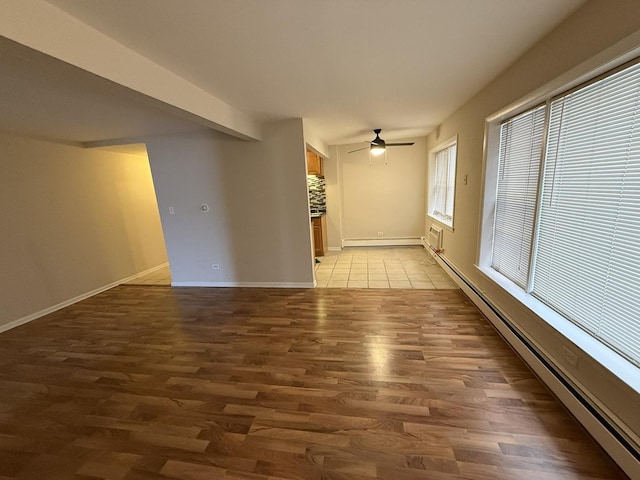 empty room featuring light wood finished floors, baseboard heating, baseboards, and ceiling fan