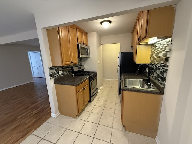 kitchen featuring a sink, dark countertops, baseboards, backsplash, and appliances with stainless steel finishes