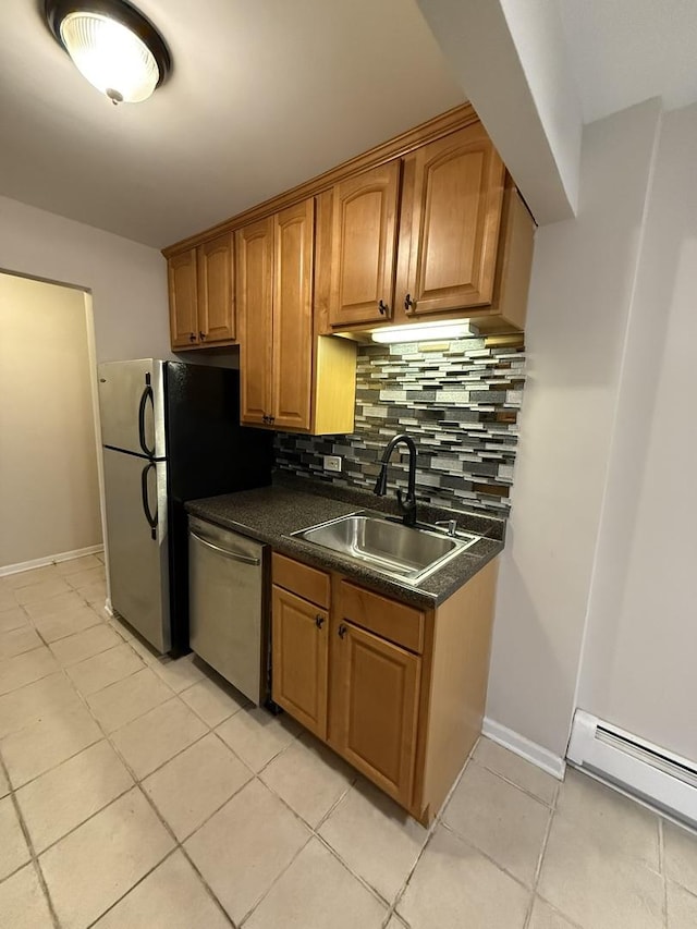 kitchen featuring dark countertops, a sink, a baseboard heating unit, light tile patterned floors, and stainless steel appliances