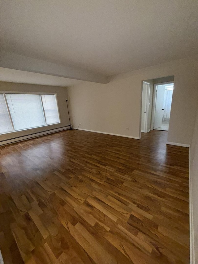 empty room with a baseboard heating unit, baseboards, and wood finished floors
