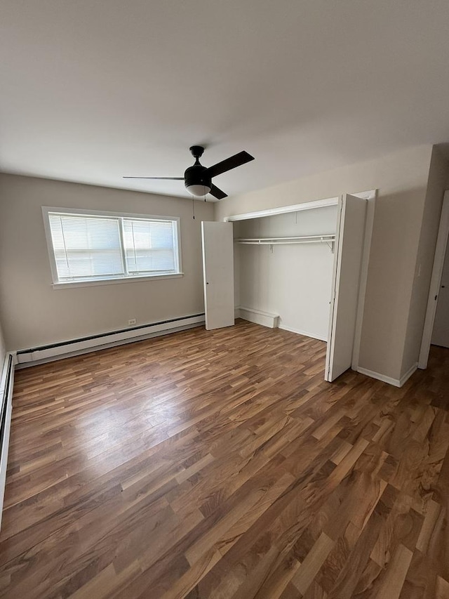 unfurnished bedroom with baseboards, baseboard heating, wood finished floors, a ceiling fan, and a closet
