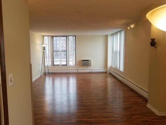 5401 S Hyde Park Blvd Unit 705, Chicago, IL 60615 - empty room featuring a baseboard radiator, a wall mounted AC, wood finished floors, and baseboards
