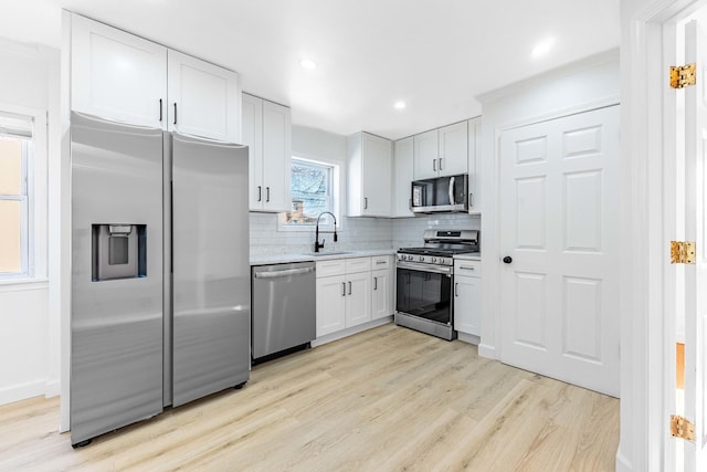 kitchen with white cabinets, stainless steel appliances, a sink, light wood-type flooring, and decorative backsplash