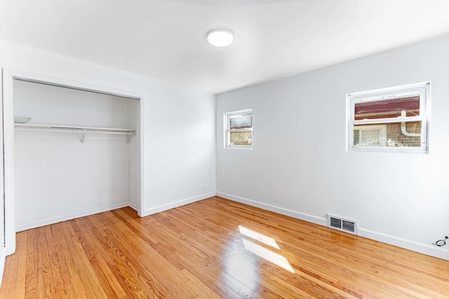unfurnished bedroom with a closet, wood finished floors, visible vents, and baseboards