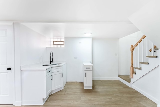 bar featuring baseboards, a sink, light wood-style floors, and stairway