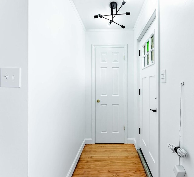 entryway with baseboards, crown molding, a chandelier, and light wood-style flooring