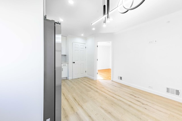 empty room with light wood-type flooring, visible vents, ornamental molding, and a barn door