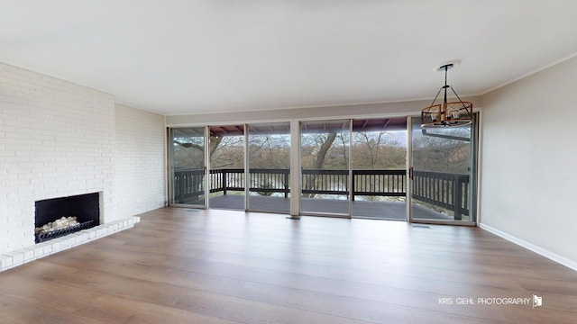 unfurnished living room featuring a chandelier, a brick fireplace, wood finished floors, and baseboards