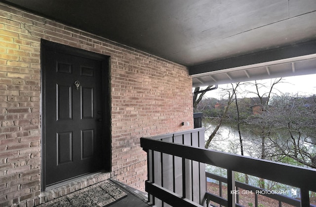 doorway to property featuring brick siding, a water view, and a balcony