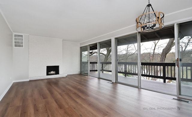 unfurnished living room featuring a chandelier, wood finished floors, a fireplace, baseboards, and ornamental molding