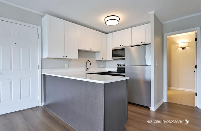 kitchen with stainless steel appliances, a peninsula, white cabinetry, and light countertops