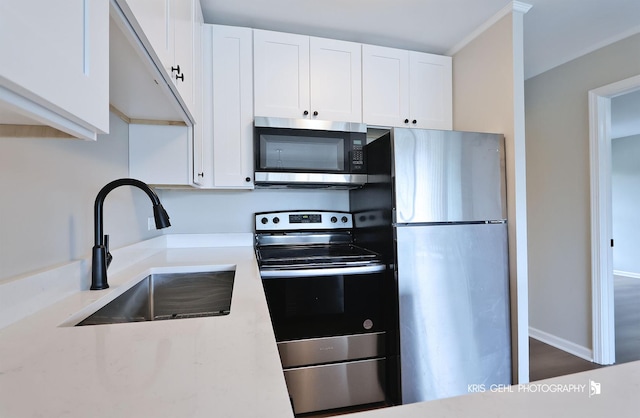 kitchen with stainless steel appliances, a sink, white cabinets, and baseboards