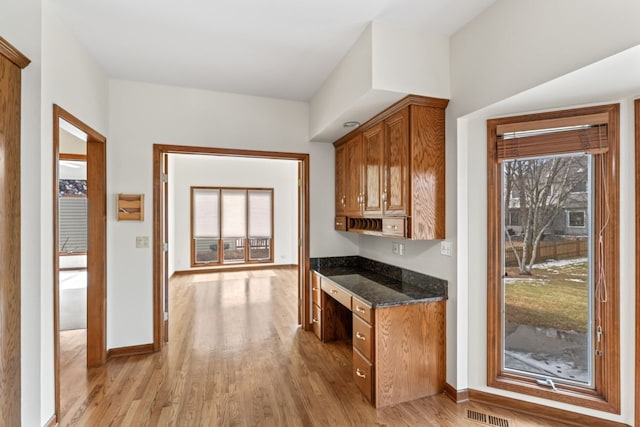 kitchen with baseboards, light wood-style flooring, dark stone counters, and brown cabinetry