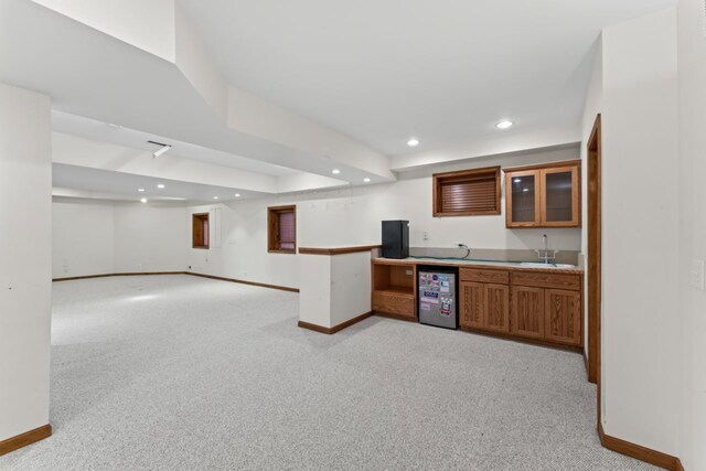 kitchen with light colored carpet, brown cabinetry, baseboards, and a sink