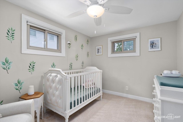 bedroom with baseboards, light carpet, a ceiling fan, and a crib