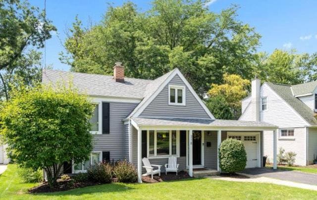 view of front facade with a garage, a front lawn, aphalt driveway, covered porch, and a chimney