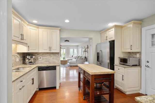 kitchen with cream cabinets, light stone countertops, a sink, stainless steel appliances, and backsplash