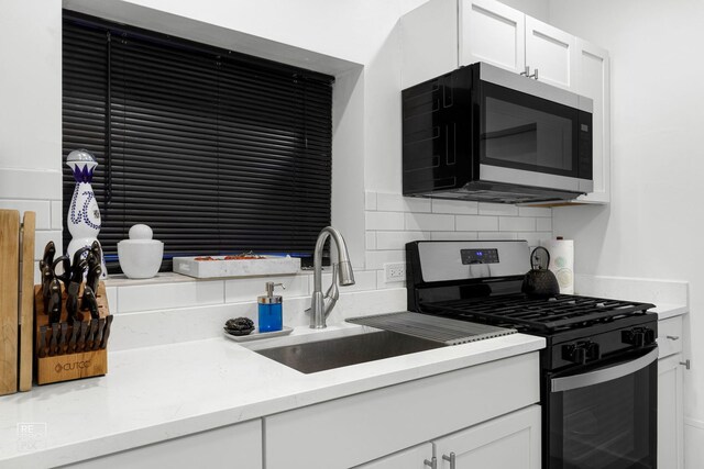 kitchen with stainless steel range with gas cooktop, a sink, backsplash, white cabinetry, and light stone countertops