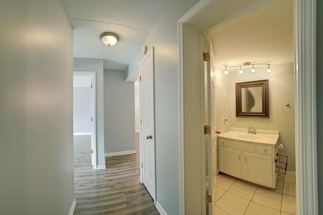 hall featuring light tile patterned floors, baseboards, and a sink