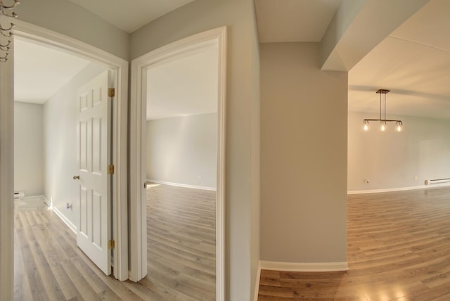 hall with a baseboard heating unit, baseboards, and light wood-style flooring