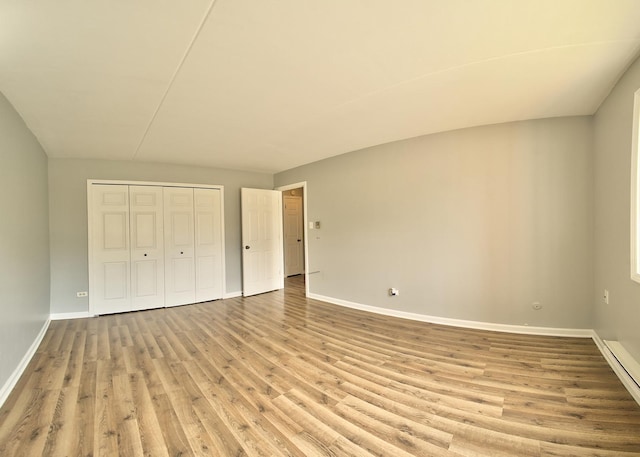 unfurnished bedroom featuring a baseboard heating unit, wood finished floors, a closet, and baseboards