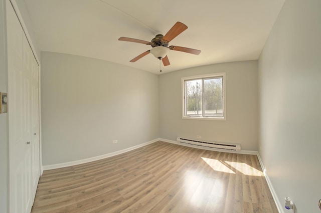 spare room featuring a baseboard radiator, baseboards, wood finished floors, and ceiling fan