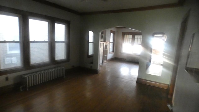 foyer entrance with radiator, arched walkways, wood finished floors, and baseboards