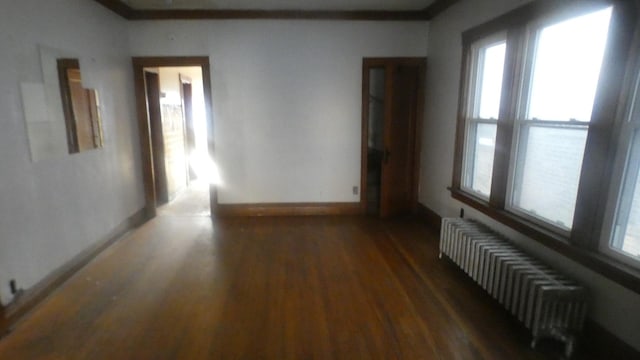 unfurnished room with radiator, a wealth of natural light, wood finished floors, and baseboards