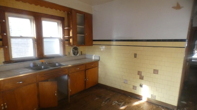 kitchen with a sink, brown cabinetry, glass insert cabinets, tile walls, and visible vents
