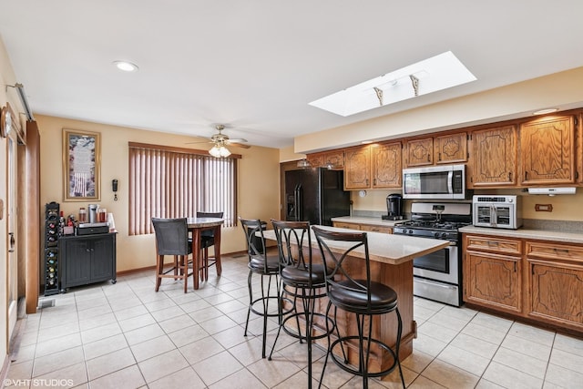 91 Frances Ln, Chicago Heights, IL 60411 - kitchen with a kitchen breakfast bar, a skylight, appliances with stainless steel finishes, brown cabinets, and light tile patterned floors