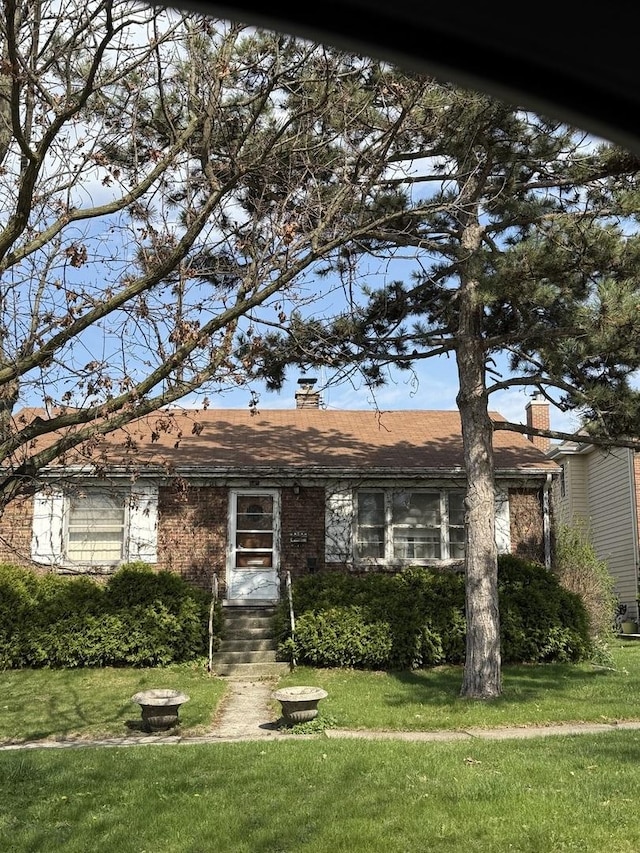 ranch-style house with brick siding, a chimney, and a front lawn