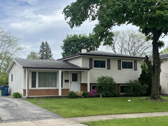 split level home with brick siding, a front yard, and a chimney