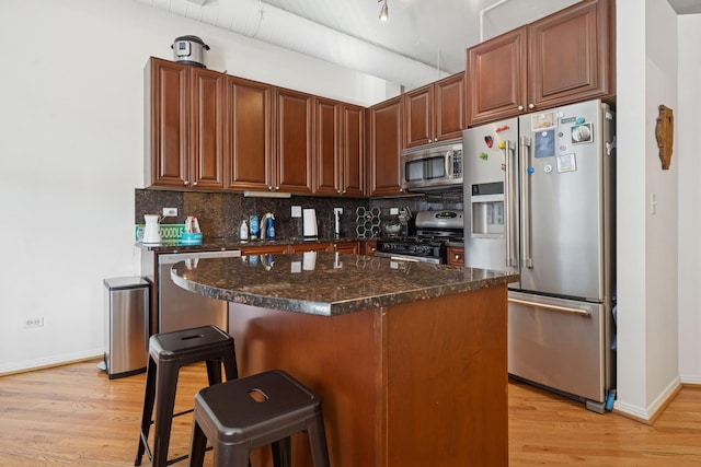 kitchen with backsplash, appliances with stainless steel finishes, light wood-type flooring, baseboards, and a breakfast bar