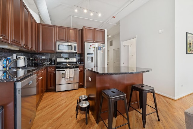 kitchen with a kitchen island, a breakfast bar, a sink, light wood finished floors, and stainless steel appliances