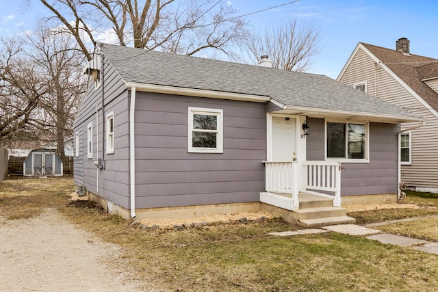 bungalow-style house with a shed, a shingled roof, a chimney, an outbuilding, and a front lawn