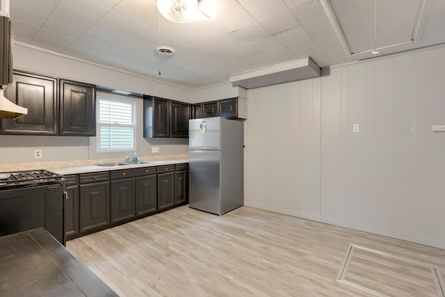 kitchen featuring freestanding refrigerator, black range with gas stovetop, a sink, light wood-style flooring, and dark brown cabinetry
