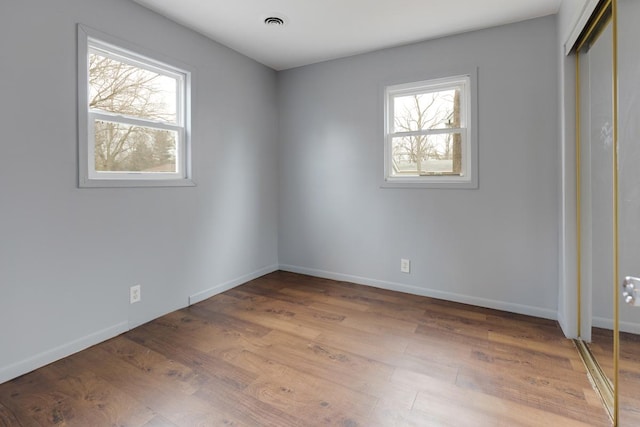 unfurnished bedroom featuring multiple windows, wood finished floors, baseboards, and a closet