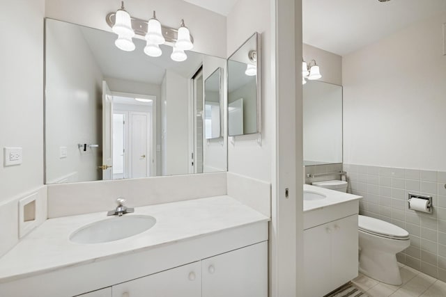 bathroom featuring tile patterned floors, toilet, vanity, tile walls, and wainscoting
