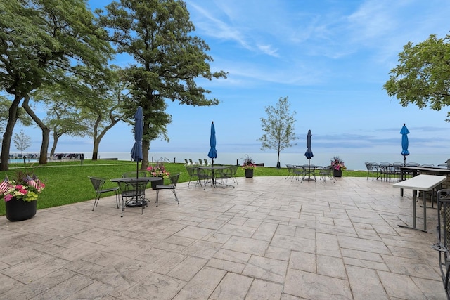 view of community featuring a patio area, a water view, outdoor dining space, and a lawn