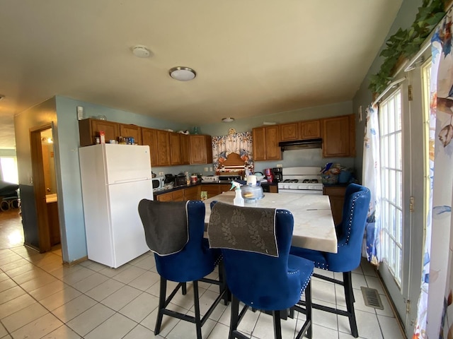 kitchen featuring brown cabinets, under cabinet range hood, light tile patterned floors, visible vents, and white appliances