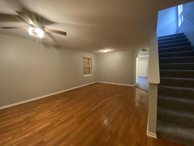 empty room featuring baseboards, wood finished floors, ceiling fan, and stairs