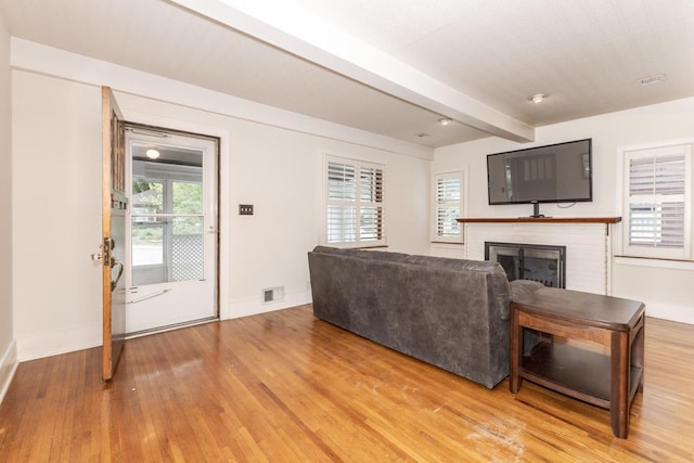 living area featuring light wood-style floors, a brick fireplace, baseboards, and beam ceiling