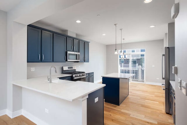 kitchen featuring appliances with stainless steel finishes, a kitchen island, a sink, light wood-style floors, and light countertops