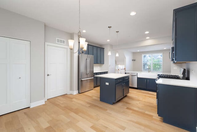 kitchen featuring appliances with stainless steel finishes, a center island, light countertops, light wood-style flooring, and blue cabinetry