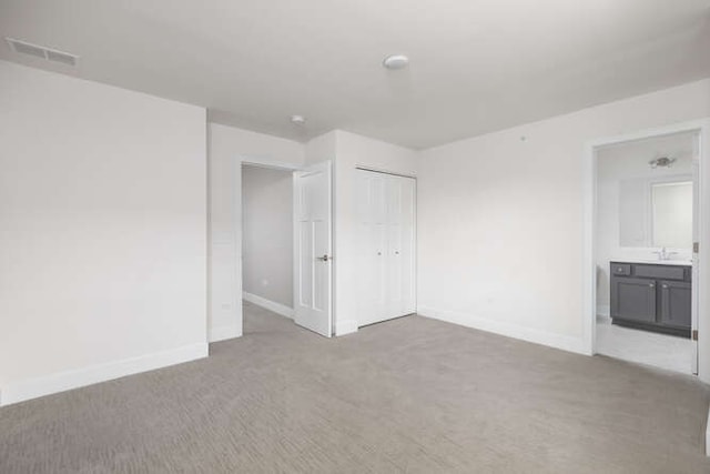 unfurnished bedroom featuring carpet flooring, baseboards, a closet, a sink, and ensuite bathroom