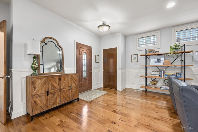 entrance foyer featuring a wainscoted wall, a decorative wall, and light wood-type flooring
