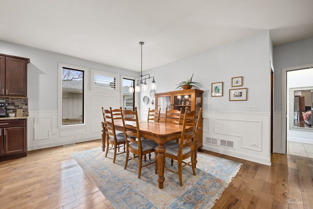 dining space featuring a wainscoted wall, visible vents, light wood-style flooring, and a decorative wall